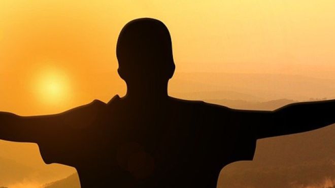 Person with arms outstretched facing an orange sky