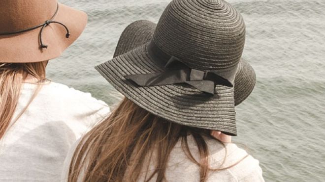 Two women in straw hats facing a body of water
