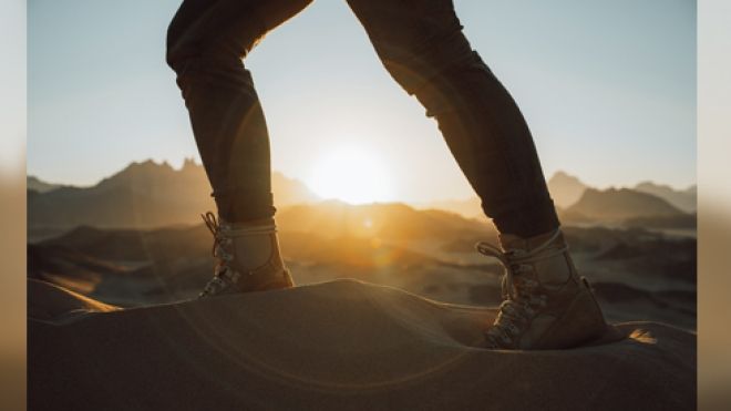 Feet walking in the desert wilderness with sun cresting the horizon
