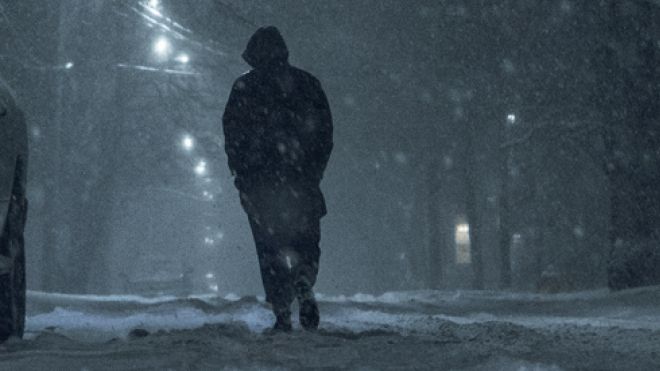Person walking in the snow on an urban street at night