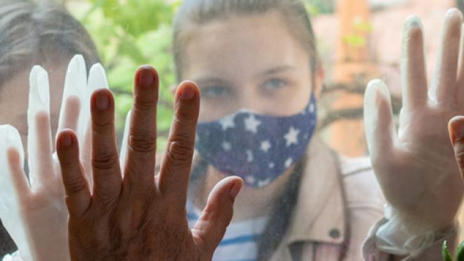 Masked people meeting with hands pressed against a window