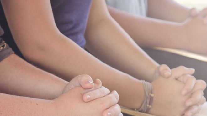 A row of hands clasped in prayer