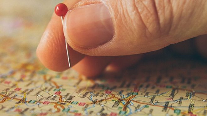 world map with a hand putting a red pin on a location