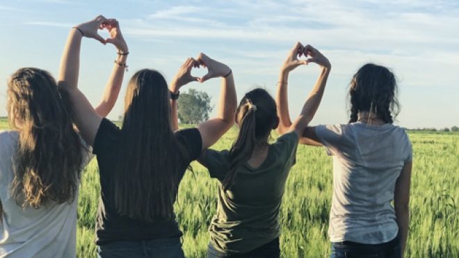 Friends linking arms and making hand hearts silhoutted on a grassy meadow