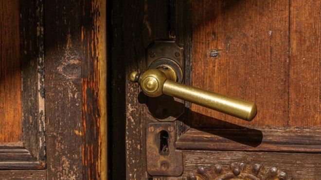 A brass door handle on an old wooden door