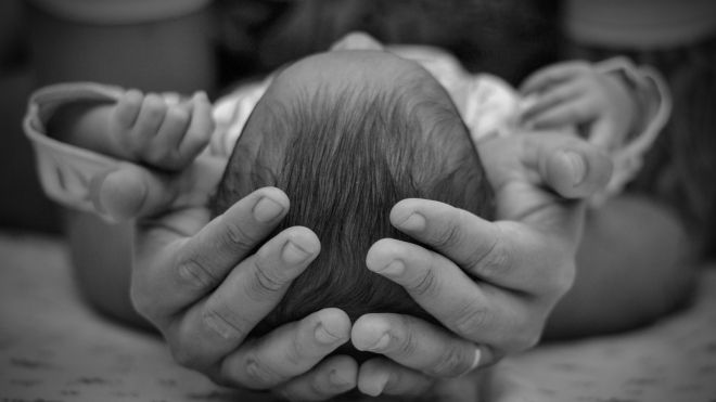 A black and white photo of the top of a newborn's head resting in an adult's palms