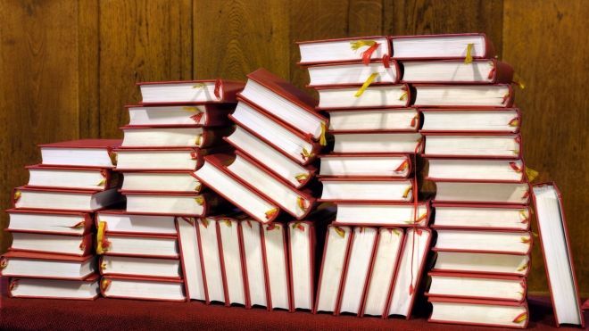 Messy stacks of red hymnals against a wood-panelled wall