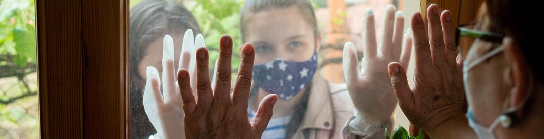 Masked people meeting with hands pressed against a window