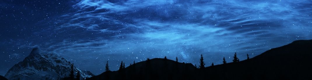starry sky with low mountians and trees in silhouette