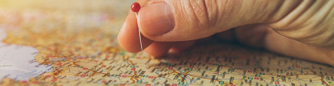 world map with a hand putting a red pin on a location