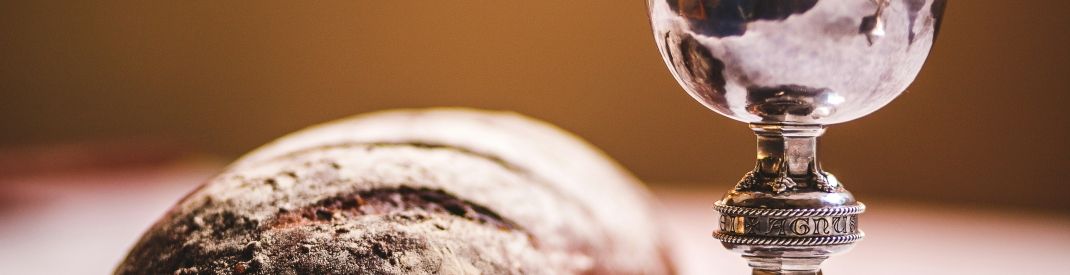 A rustic loaf and a silver cup on a white table