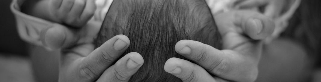 A black and white photo of the top of a newborn's head resting in an adult's palms