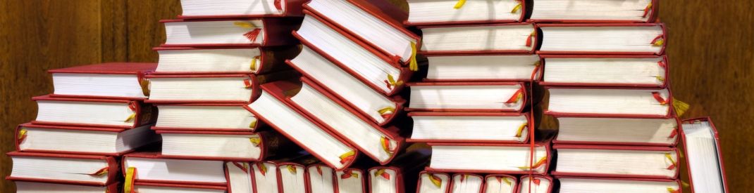 Messy stacks of red hymnals against a wood-panelled wall